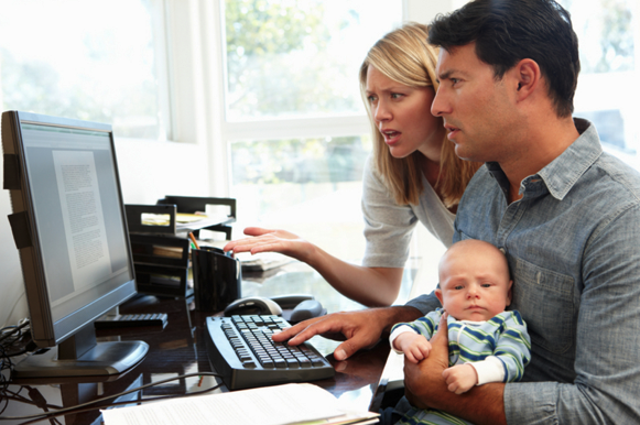 parents searching on the computer for a preschool while the father is holding their baby